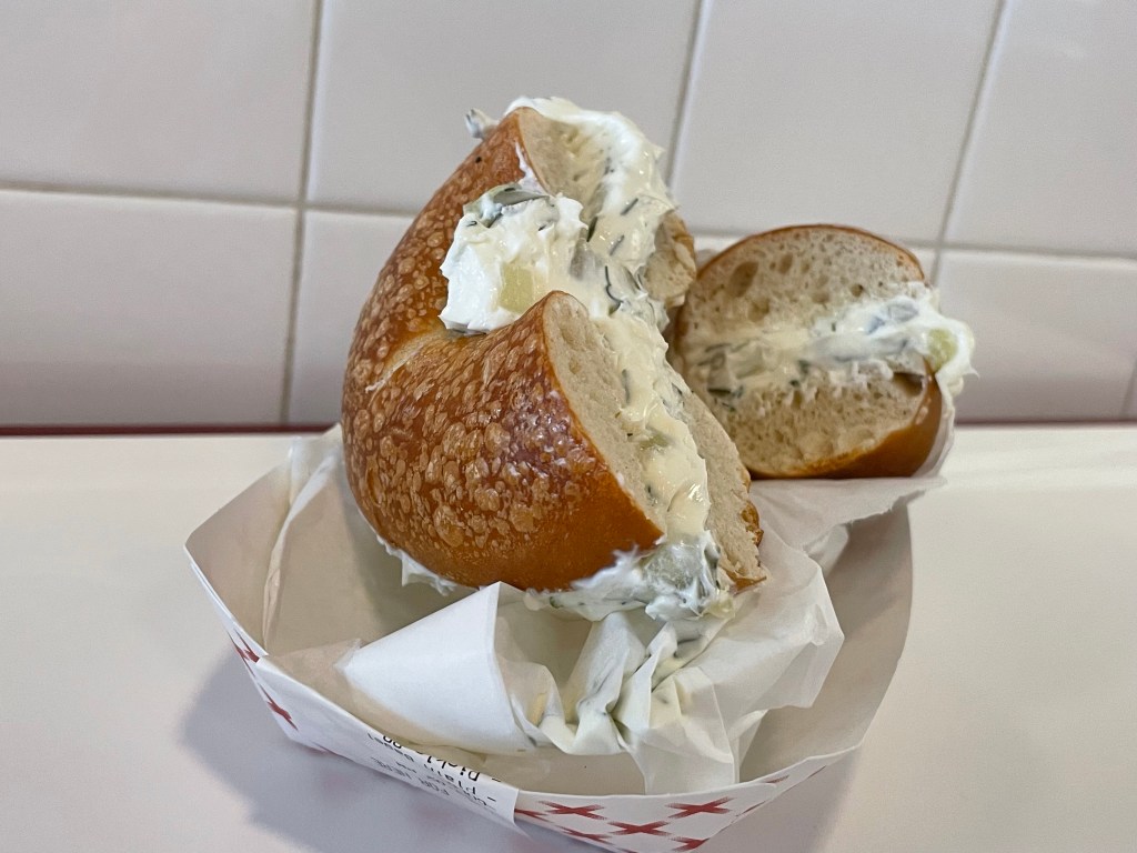 A bagel sliced in half filled with cream cheese sits atop a white and red picnic tray.